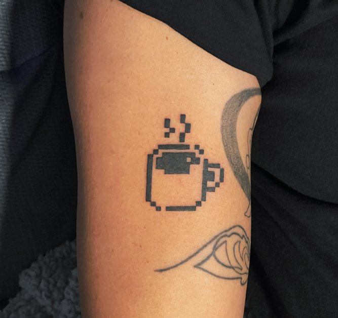Pixel art coffee cup tattoo in black on an upper arm